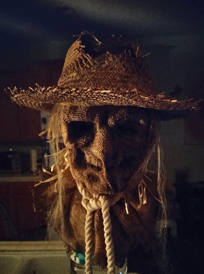 A spooky scarecrow mask wearing a straw hat for creepy Halloween homes decoration.