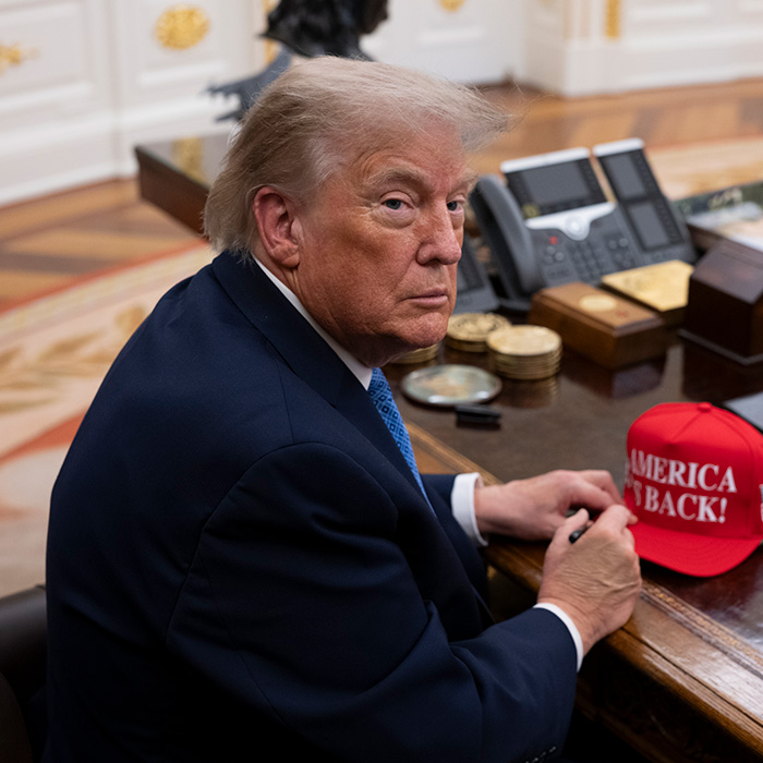Donald Trump sitting at desk with a red America is Back hat Donald Trump sitting at desk with a red America is Back hat