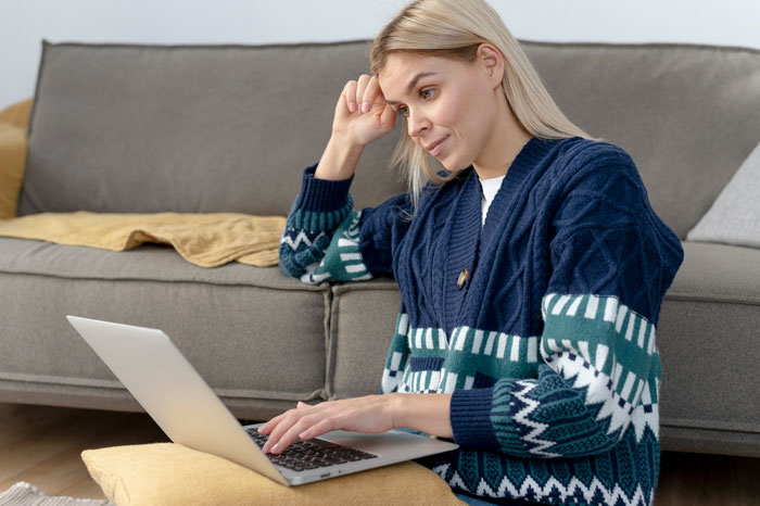A young blonde woman sitting on the floor using a laptop to research recovering from surgery.