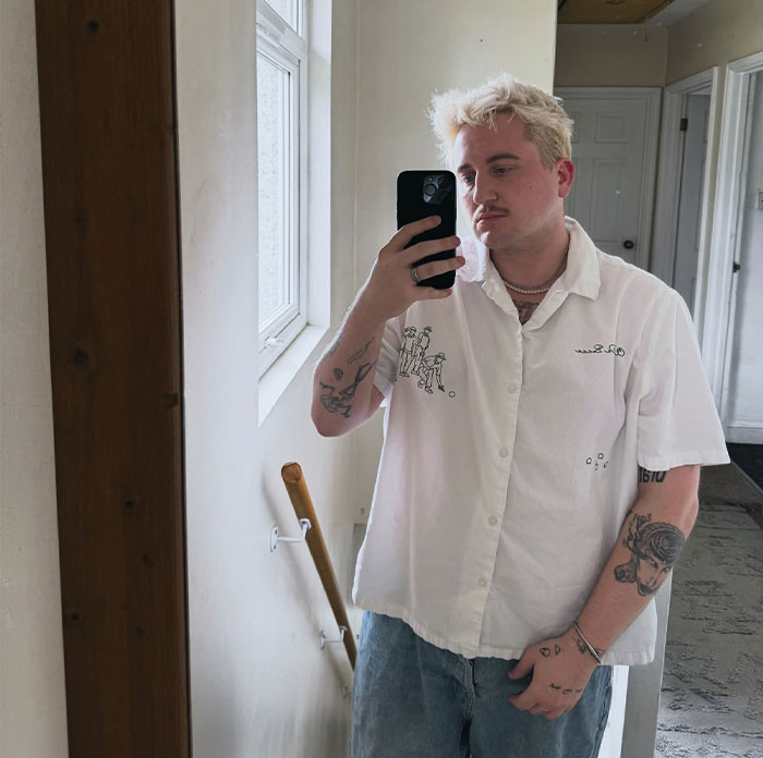 Man taking mirror selfie with tattoos wearing white shirt