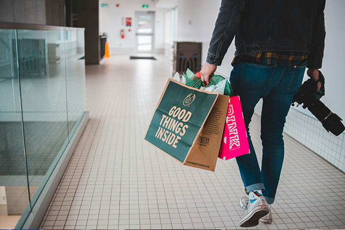 Man carrying shopping bags walking indoors with camera in hand
