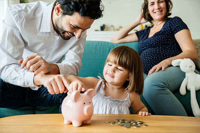 Family teaching child saving money using piggy bank at home