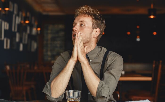 A man sitting at a bar with hands pressed together, sensing something was off.