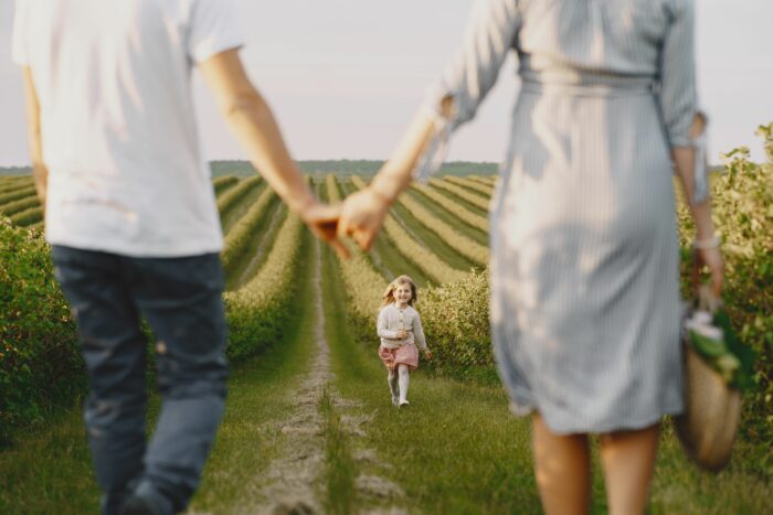 Family holding hands with child running toward them in field Family holding hands with child running toward them in field