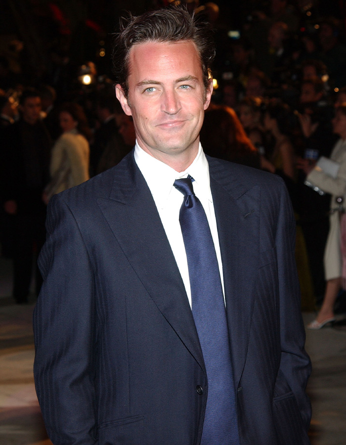 Matthew Perry in a navy suit and tie attending a formal red carpet event.