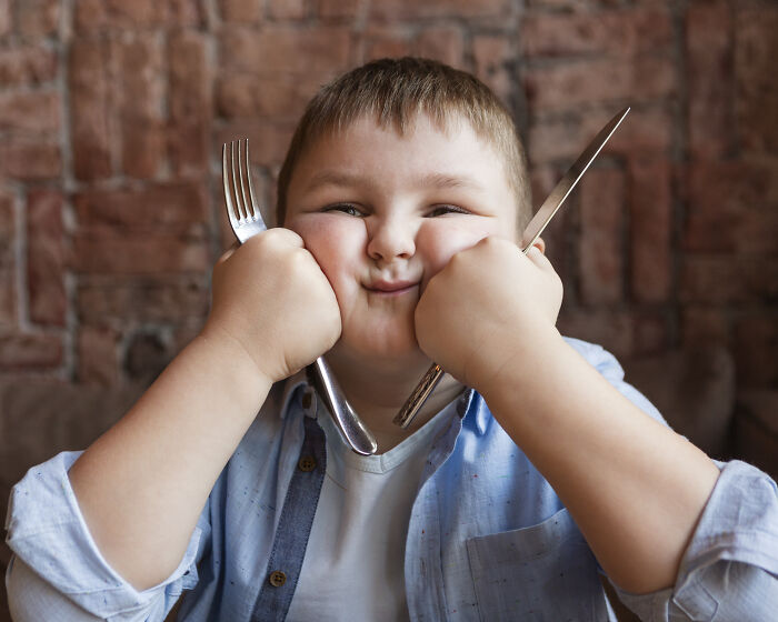 A young boy with chubby cheeks holding a fork and knife, representing early onset health problems in Gen Z.