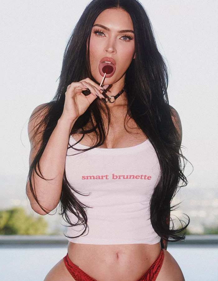Megan Fox holding a lollipop and wearing a smart brunette crop top in a photoshoot.