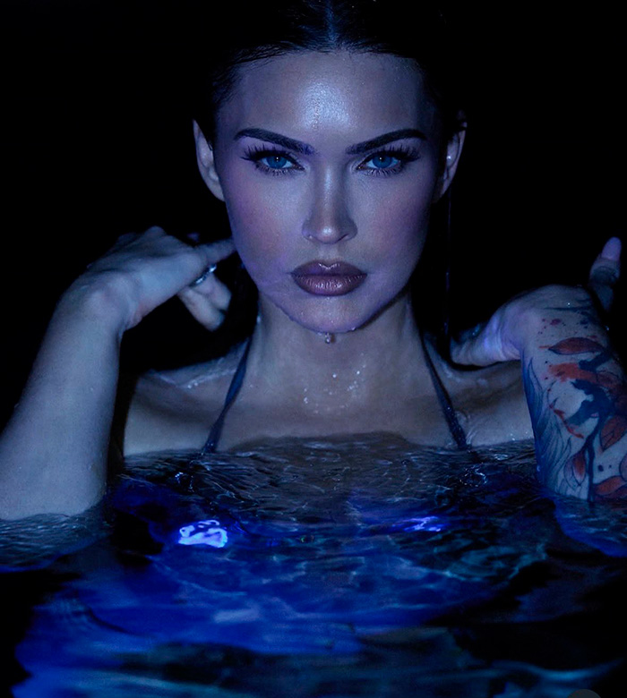 Megan Fox submerged in dark blue water looking directly at the camera.