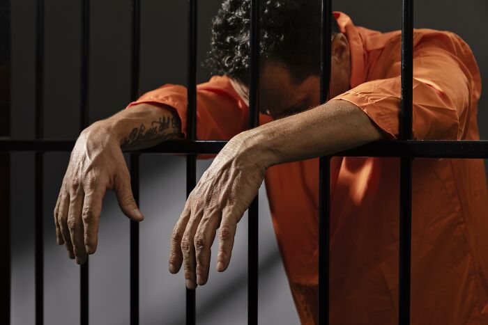 A prisoner behind bars leaning in despair, illustrating getting disowned by family