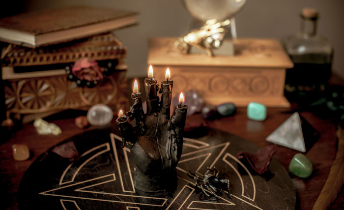 Black hand-shaped candle burning on occult altar with crystals and wooden boxes Black hand-shaped candle burning on occult altar with crystals and wooden boxes
