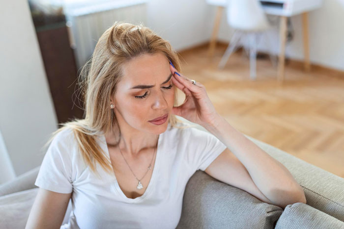 Woman with headache sitting on couch looking distressed Woman with headache sitting on couch looking distressed