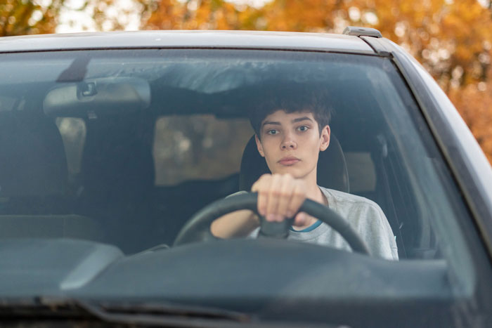 A teen boy sits behind the steering wheel of his first car A teen boy sits behind the steering wheel of his first car