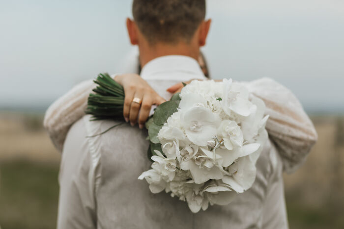 A bride holding a white flower bouquet while hugging the groom, taken from a wedding before a divorce.
