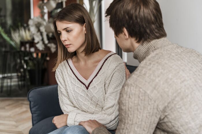 A man trying to comfort an upset woman sitting on a couch, showing relationship struggles of divorced people