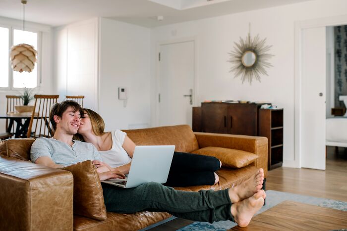 A happy couple relaxing on a leather sofa before wedding plans with a laptop.