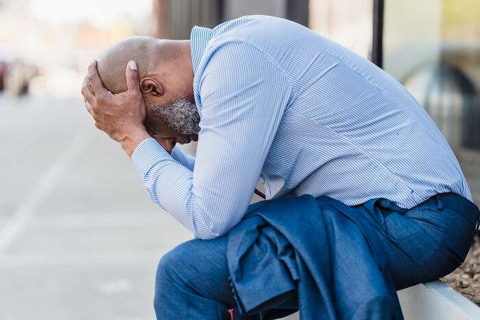 A distressed man sitting outdoors holding his head in hands, coping with difficulty before divorce.