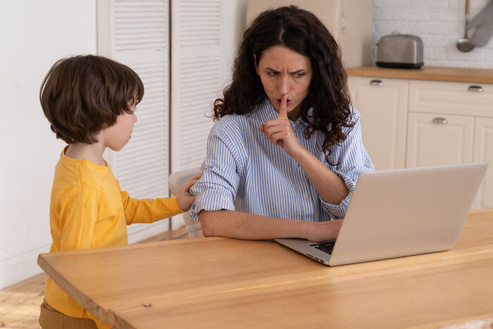 A busy mother hushing her child while working, illustrating challenges discussed by divorced people.
