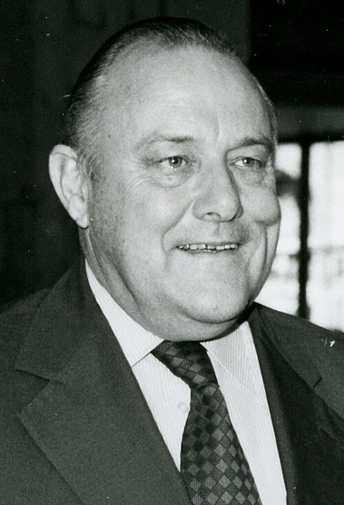 A black and white portrait of a smiling older man, illustrating clever wit and intelligent insults.