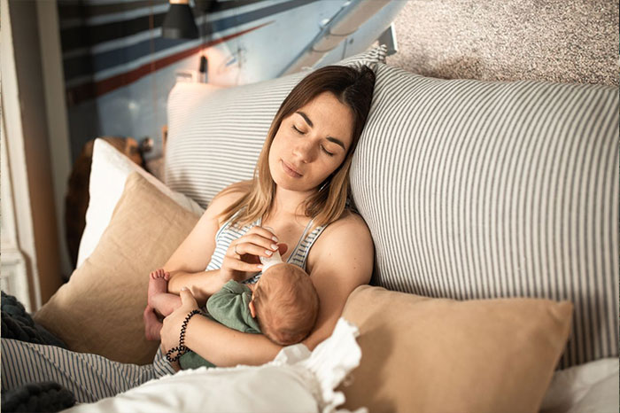Mother feeding newborn baby in bed, related to a guy pursuing ex story.