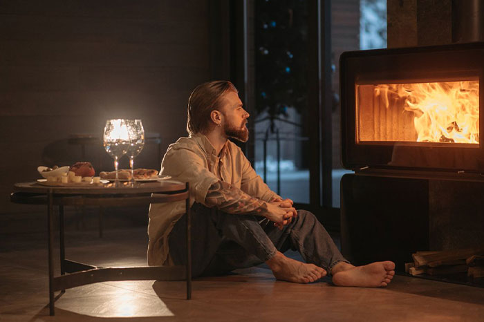 Pensive guy sitting on the floor by a burning fireplace after being rejected by his ex.
