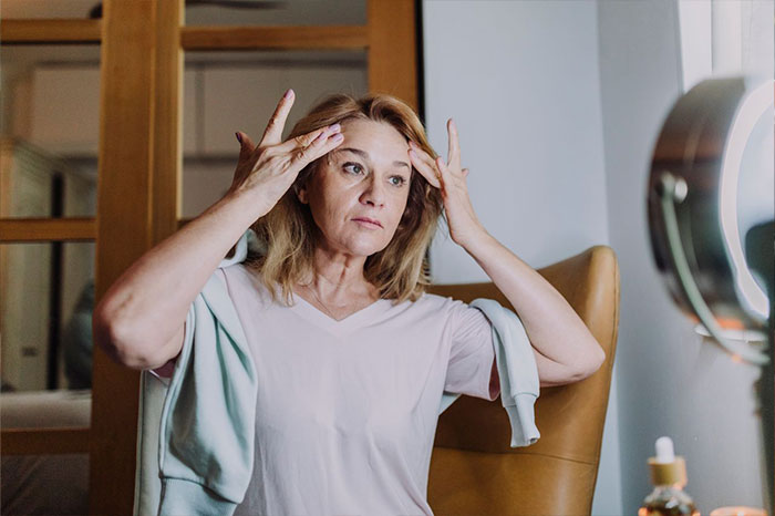 Middle-aged woman touching her face while looking in the mirror, reflecting family boundary issues.