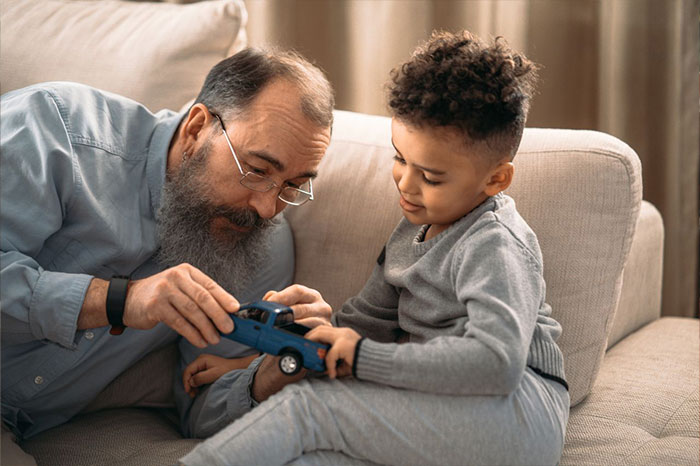 An older man with glasses showing a toy truck to a young boy on a couch.
