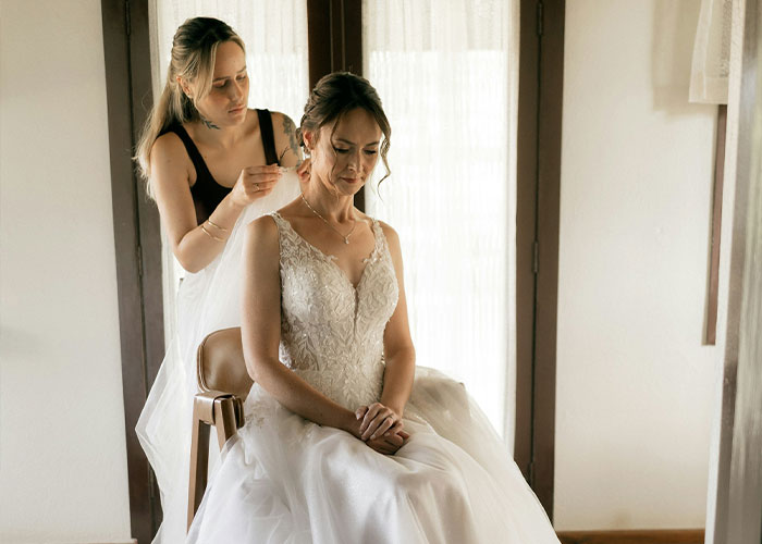 Woman helping bride put on earrings before wedding day
