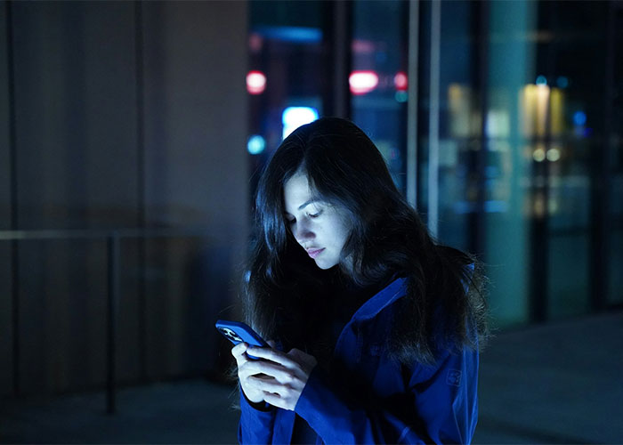 A woman looking at her mobile phone outdoors at night as a guy keeps pursuing ex who rejected him