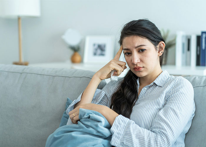 A distressed woman sitting on a couch thinking about how her sister helps her ex cross every boundary.