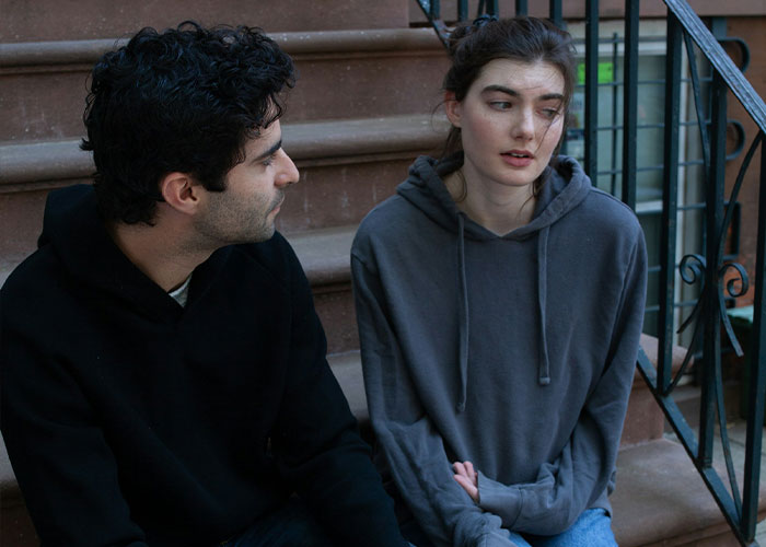 A man sitting next to a woman on steps, looking concerned while a guy keeps pursuing ex who rejected him at 18.