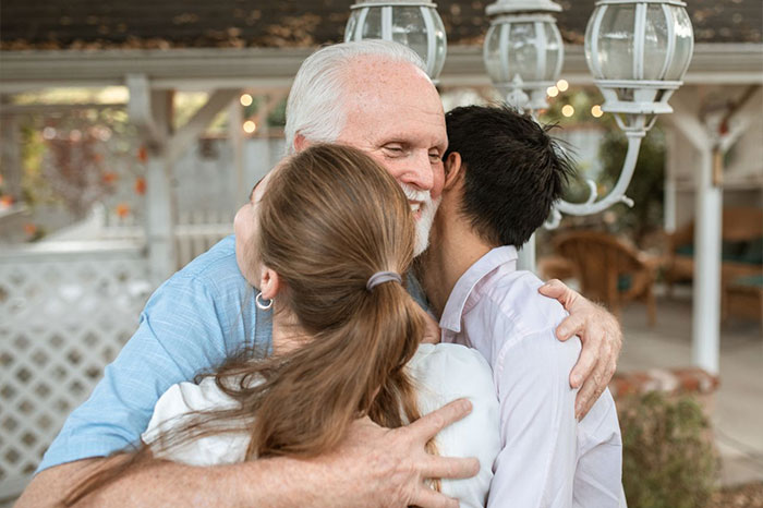 An older man hugging two younger people while discussing a guy keeps pursuing ex situation.