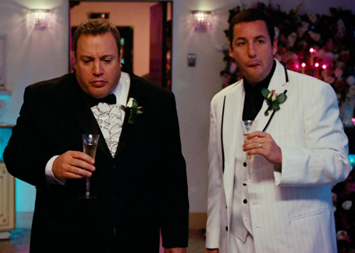 Adam Sandler with Kevin James holding champagne glasses on a movie set.