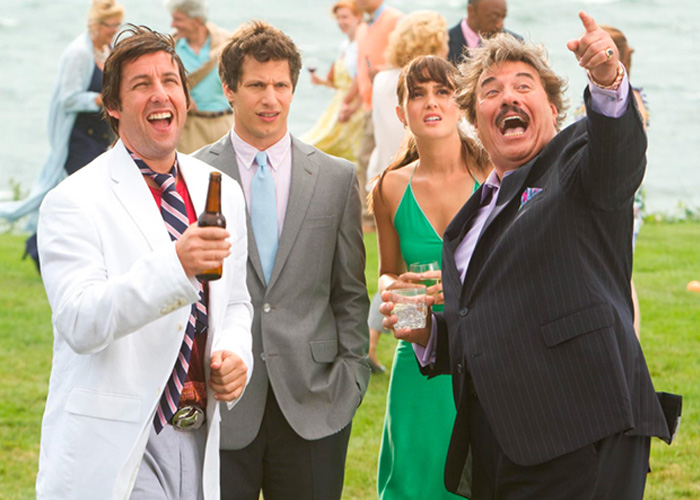 Adam Sandler holding a drink outdoors while filming a movie scene with co-stars.