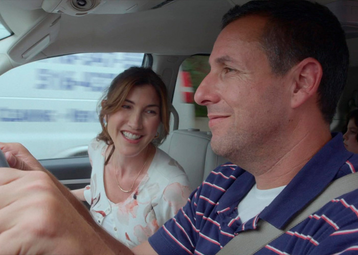 Adam Sandler driving a car with his wife Jackie smiling in the passenger seat