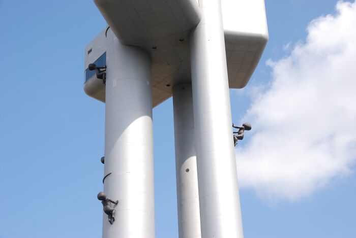 Metallic towers with human figures climbing strange buildings