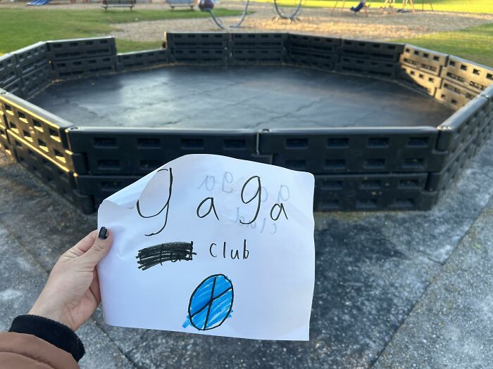 Hand holding a handwritten gaga club note near a playground pit, an example of found paper