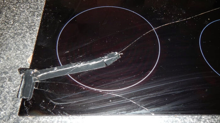 A cracked black glass stovetop taped together with black duct tape, depicting a home renovate fiasco