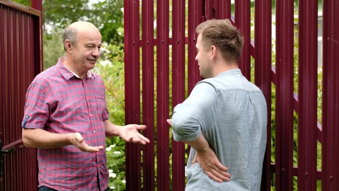 Two men talking near a red metal fence outdoors. Two men talking near a red metal fence outdoors.