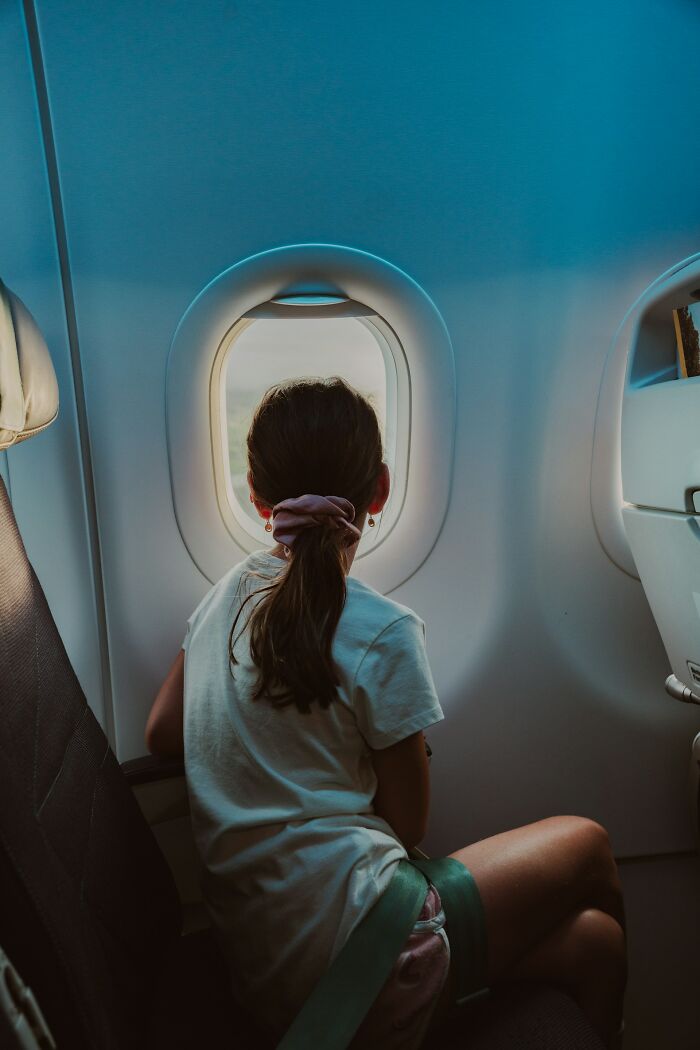 A young girl sits by an airplane window looking out during flights