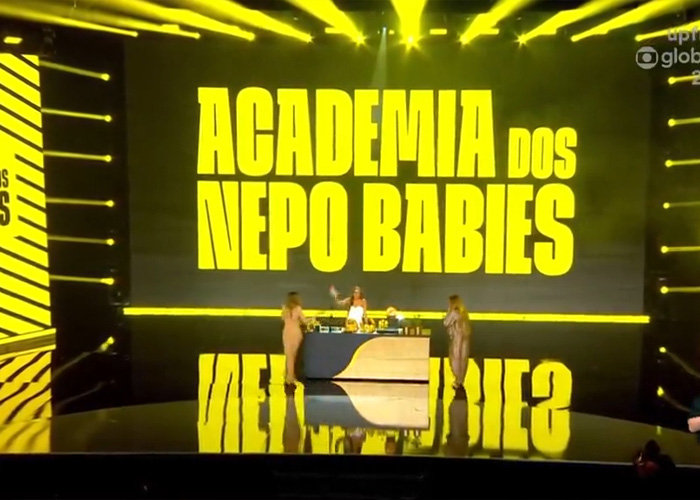 Academia Dos Nepo Babies neon sign with people on stage in reality show set Academia Dos Nepo Babies neon sign with people on stage in reality show set