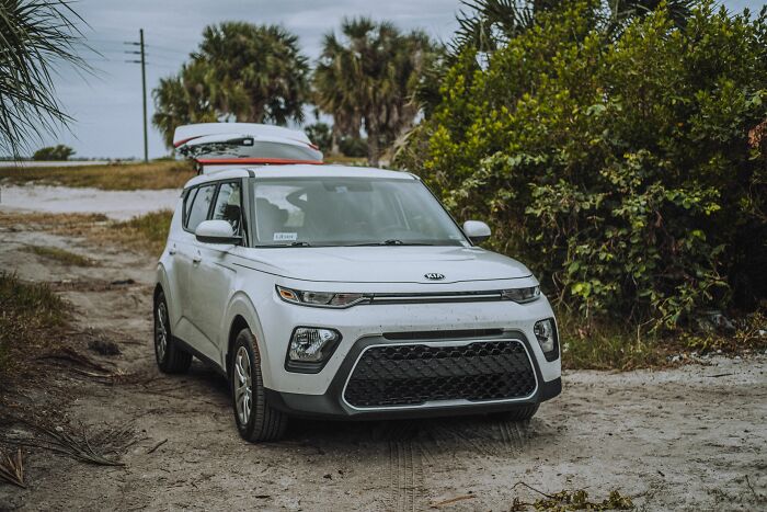 A white SUV parked on a sandy dirt path surrounded by bushes in tiny communities