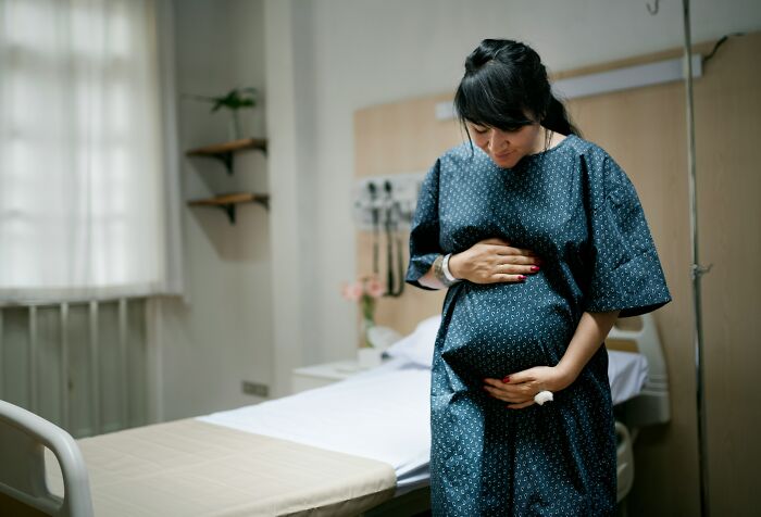 A pregnant woman holding her stomach in a hospital room in a tiny community.