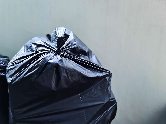 A tied black trash bag sitting outdoors in a tiny community area.