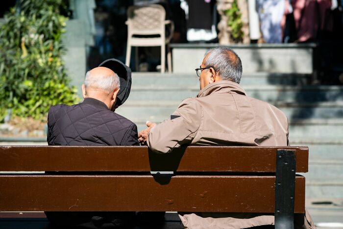 Two elderly men sitting on a park bench talking in tiny communities drama