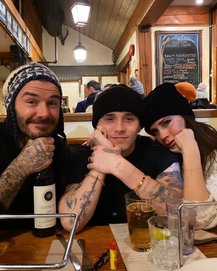 Brooklyn Beckham sitting with his parents David and Victoria Beckham at a restaurant table.