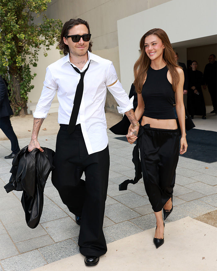 Nicola and Brooklyn Beckham walking hand-in-hand in stylish black and white outfits at an event