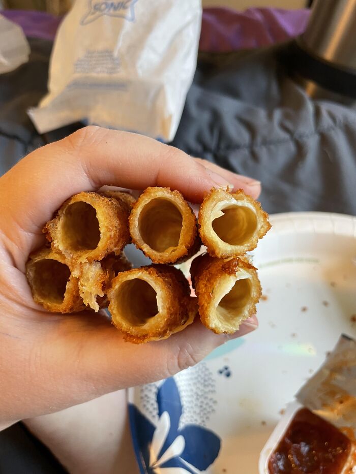 A hand holding hollow fried mozzarella sticks, showcasing one of many absurd products.