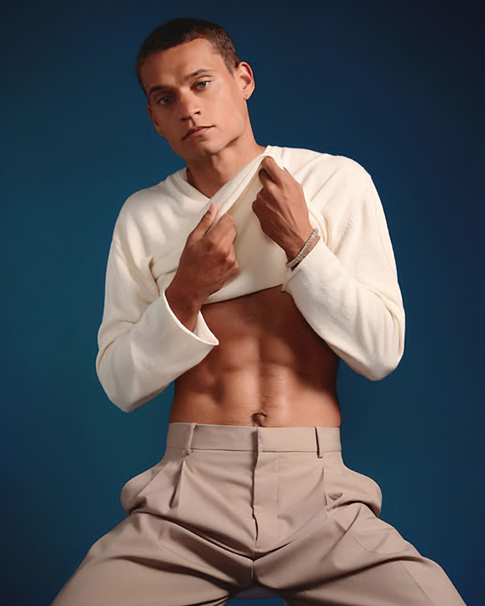 A man posing in cream sweater and pants during a Sexiest Man Alive photoshoot.