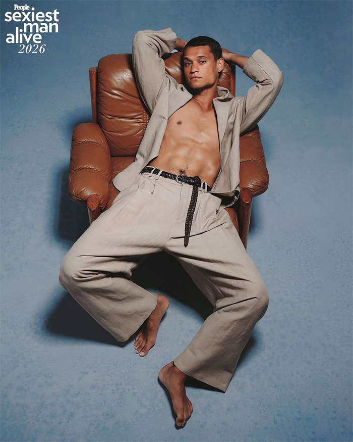 Model reclining in a leather armchair for a Sexiest Man Alive photoshoot wearing a beige suit and no shoes
