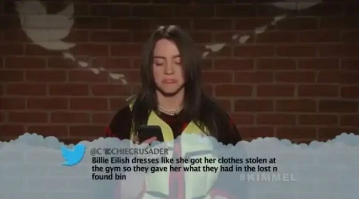 Billie Eilish reading funny insults about her clothing style during a TV show segment.
